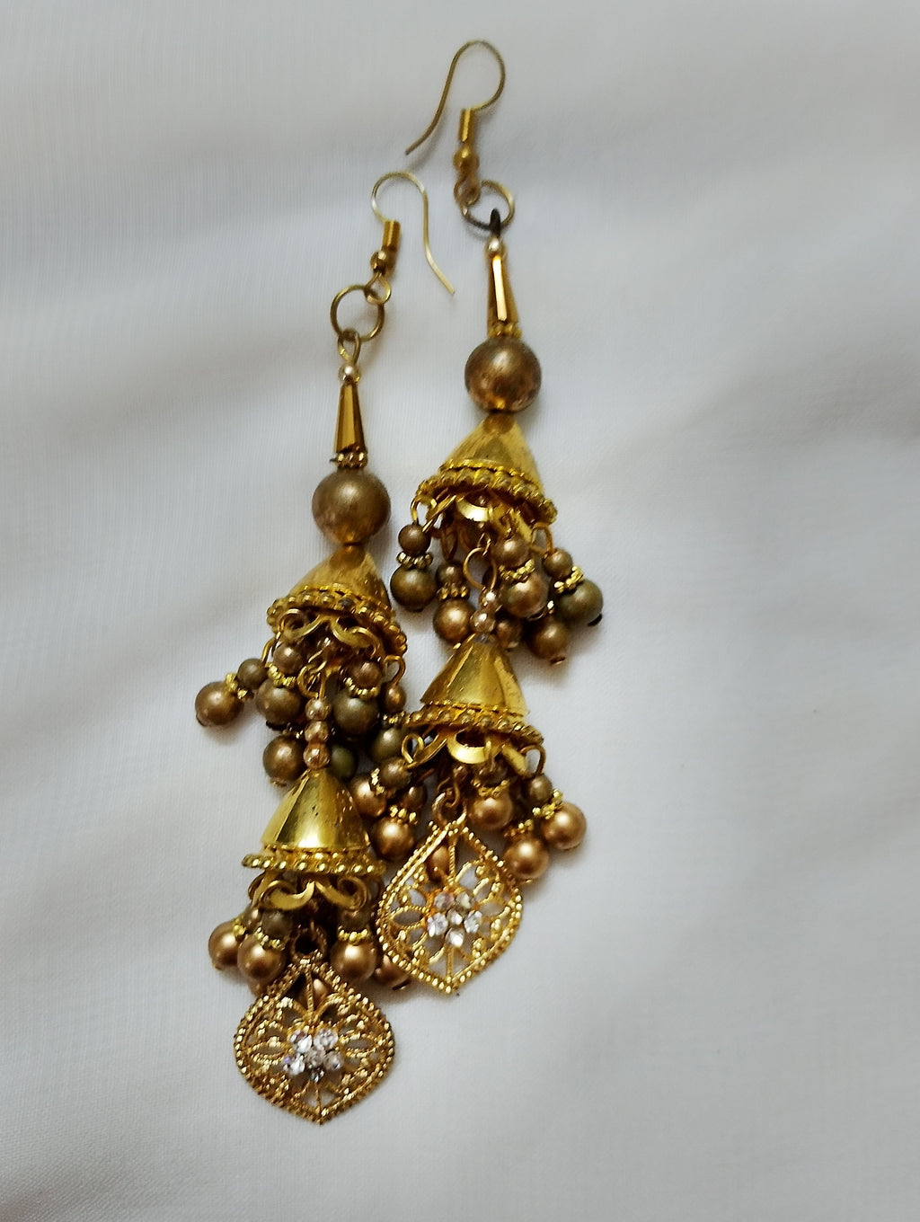 

Design The earrings feature a gold hook, a small bronze bead, a gold conical piece, a jhumka-style bell with bronze beads, and a teardrop filigree pendant inset with clear stones.